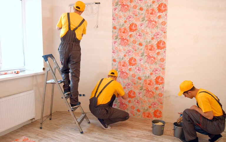 Três trabalhadores aplicando papel de parede com flores laranjas em uma parede